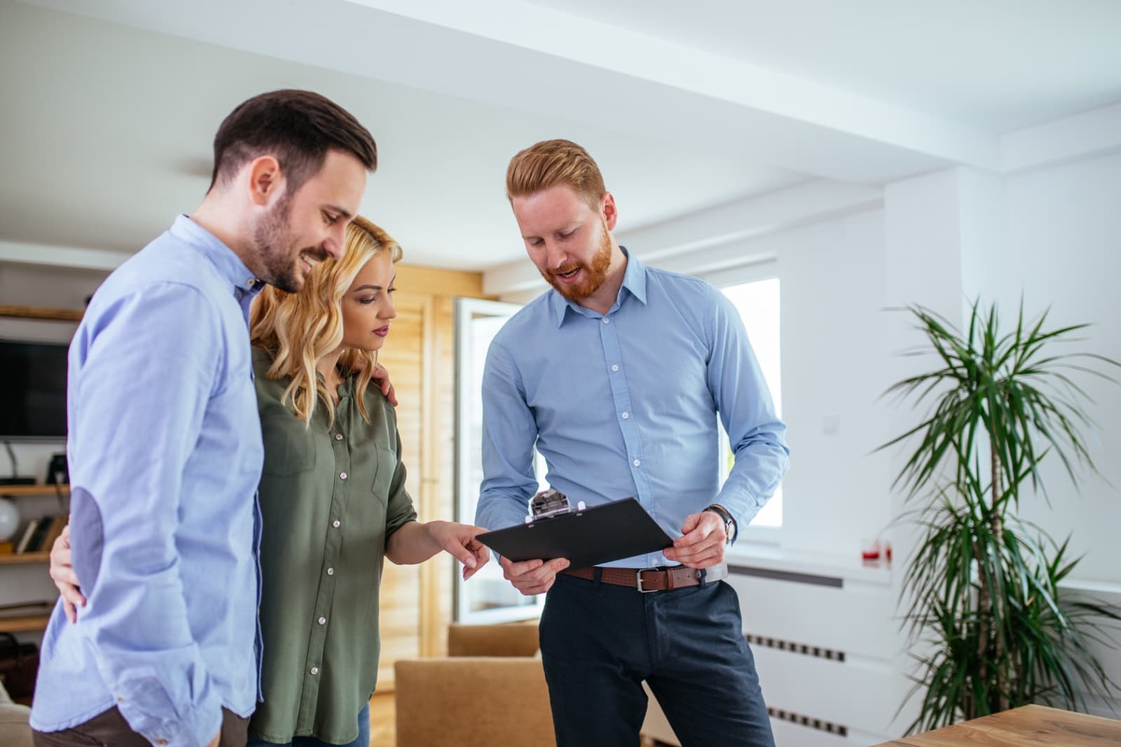 An estate agent showing a couple details on a clipboard in a bright living room