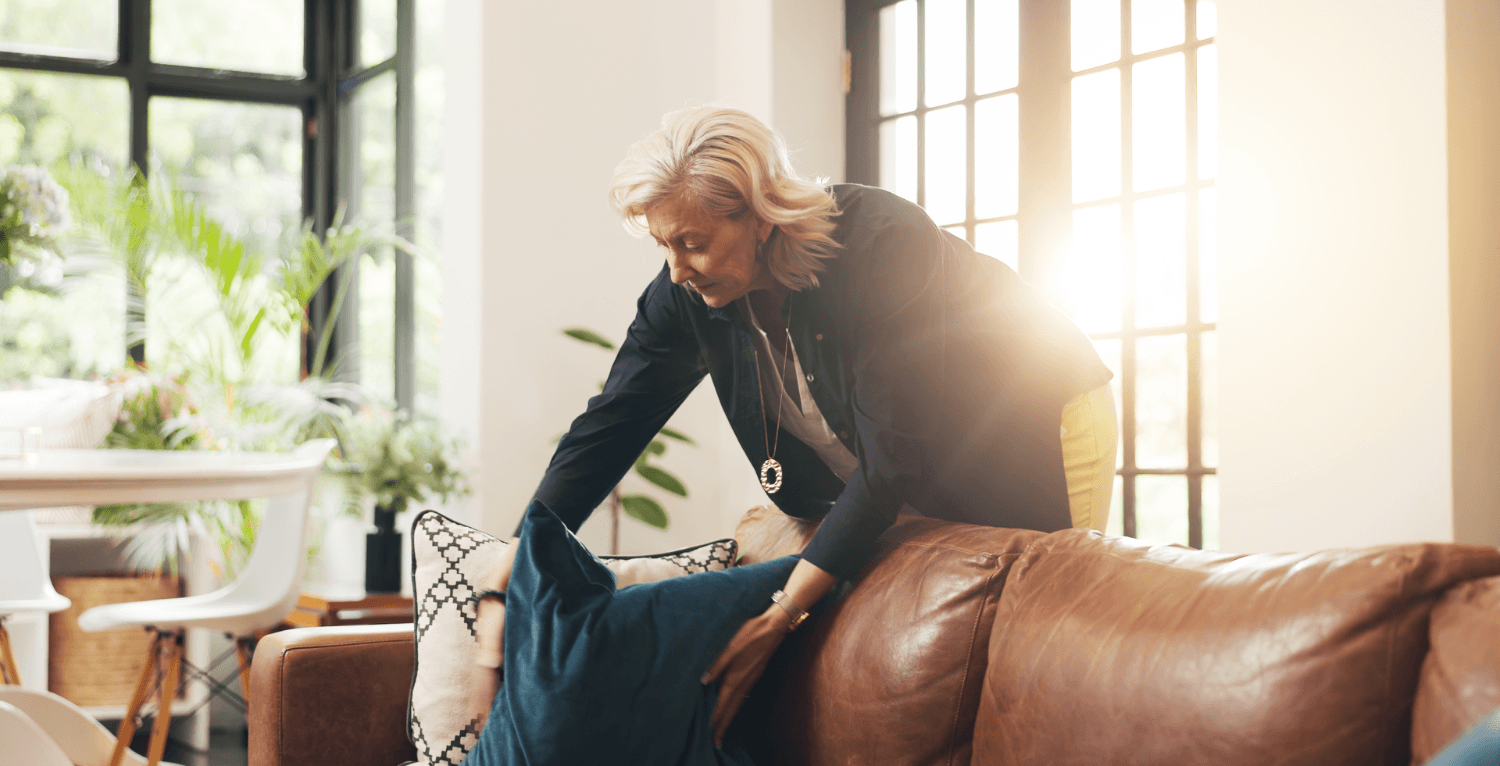 A woman plumping cushions and tidying her living room to present it for sale